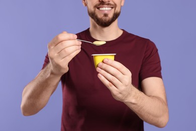 Man with tasty yogurt on purple background, closeup