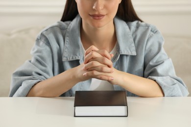 Religious woman praying over Bible at table indoors, closeup
