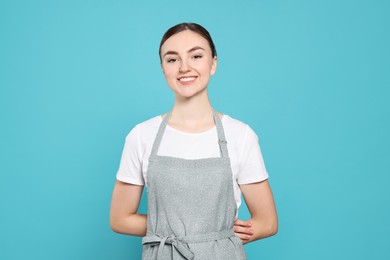 Beautiful young woman in clean apron with pattern on light blue background