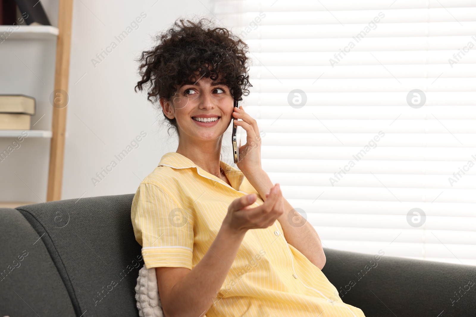 Photo of Beautiful young woman in stylish pyjama talking on smartphone on sofa at home