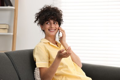 Beautiful young woman in stylish pyjama talking on smartphone on sofa at home