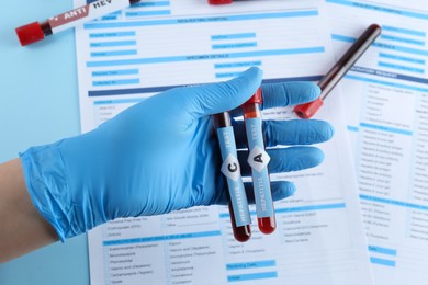 Photo of Scientist holding tubes with blood samples for hepatitis virus test near laboratory form, closeup