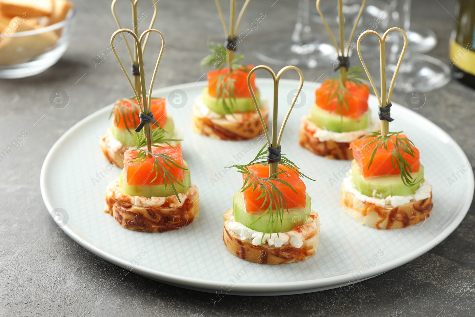 Photo of Tasty canapes with salmon, cucumber, bread and cream cheese on grey table