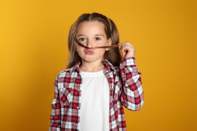 Funny little girl making fake mustache with her hair on yellow background