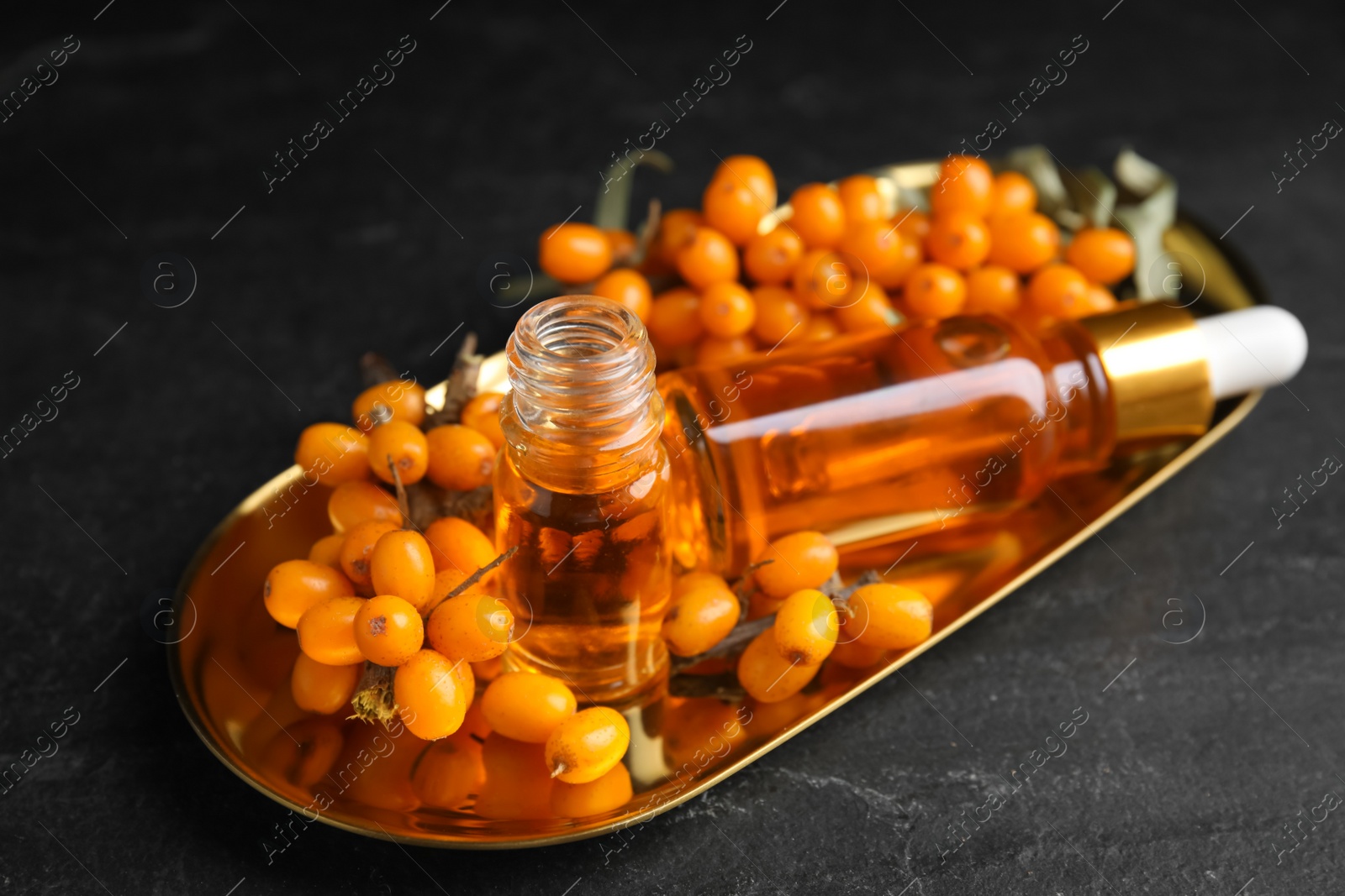 Photo of Ripe sea buckthorn and bottles of essential oil on black table