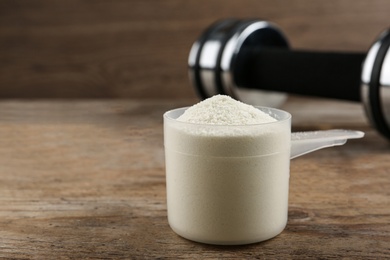 Photo of Measuring scoop of protein powder on wooden table, closeup. Space for text