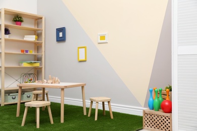 Stylish playroom interior with table, stools and green carpet