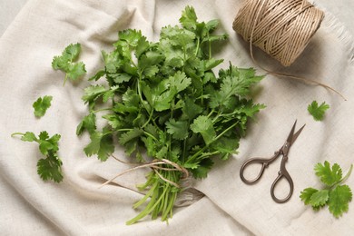 Photo of Fresh green cilantro, twine and scissors on white fabric, flat lay