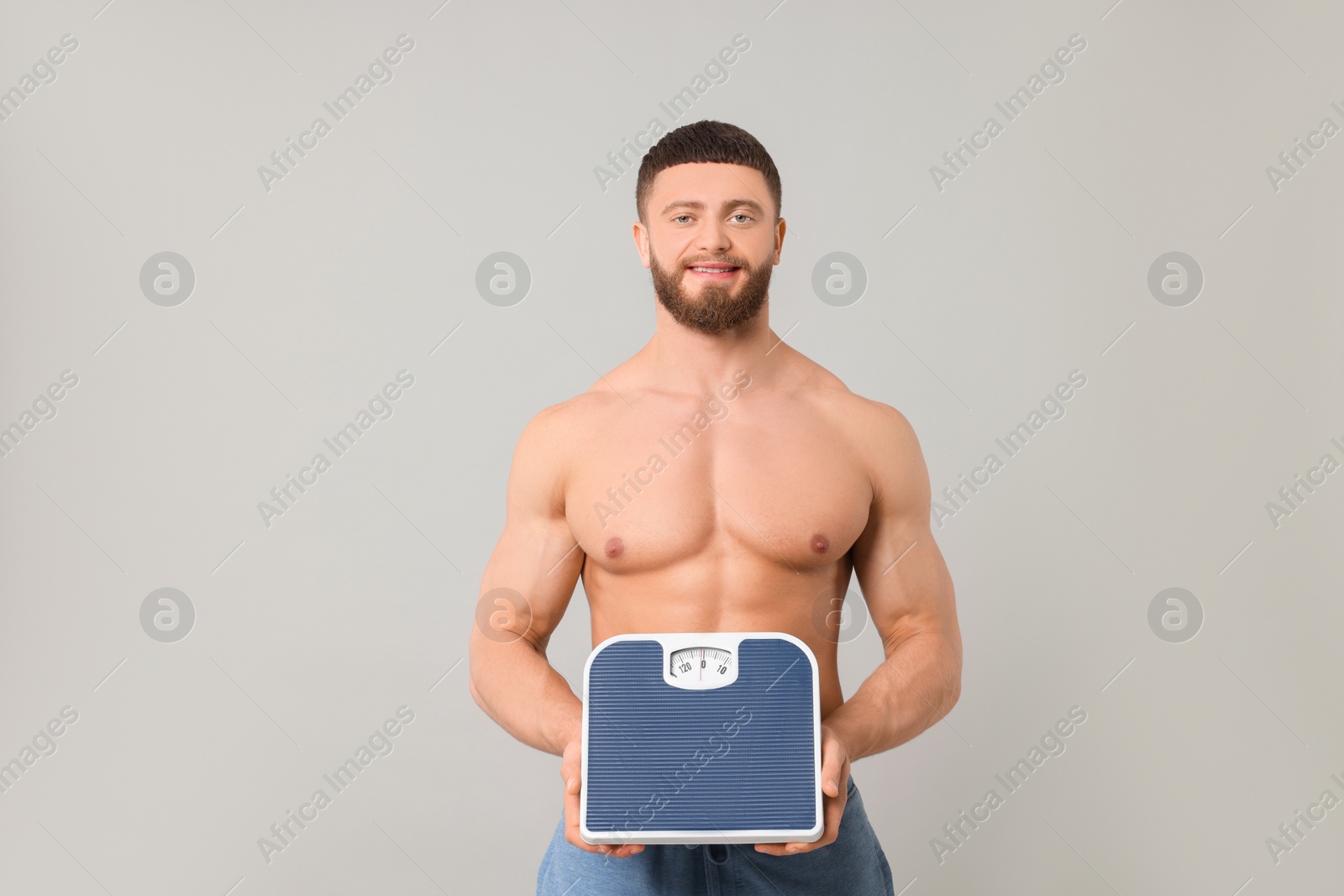 Photo of Happy athletic man holding scales on light grey background. Weight loss concept