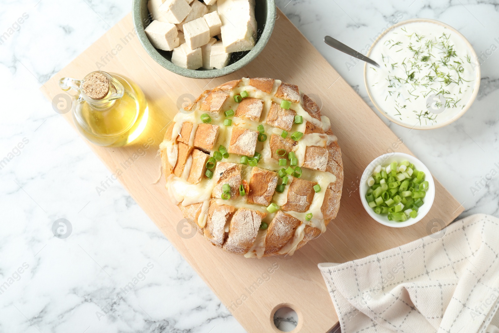 Photo of Freshly baked bread with tofu cheese and green onion served on white marble table, flat lay