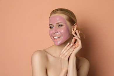 Young woman with pomegranate face mask on pale coral background