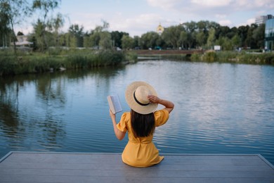 Woman reading book on pier near lake, back view