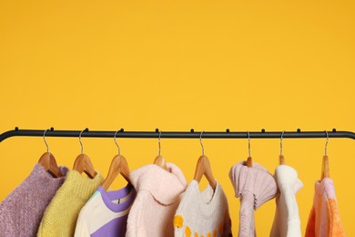 Photo of Rack with stylish women's sweaters on wooden hangers against orange background, space for text
