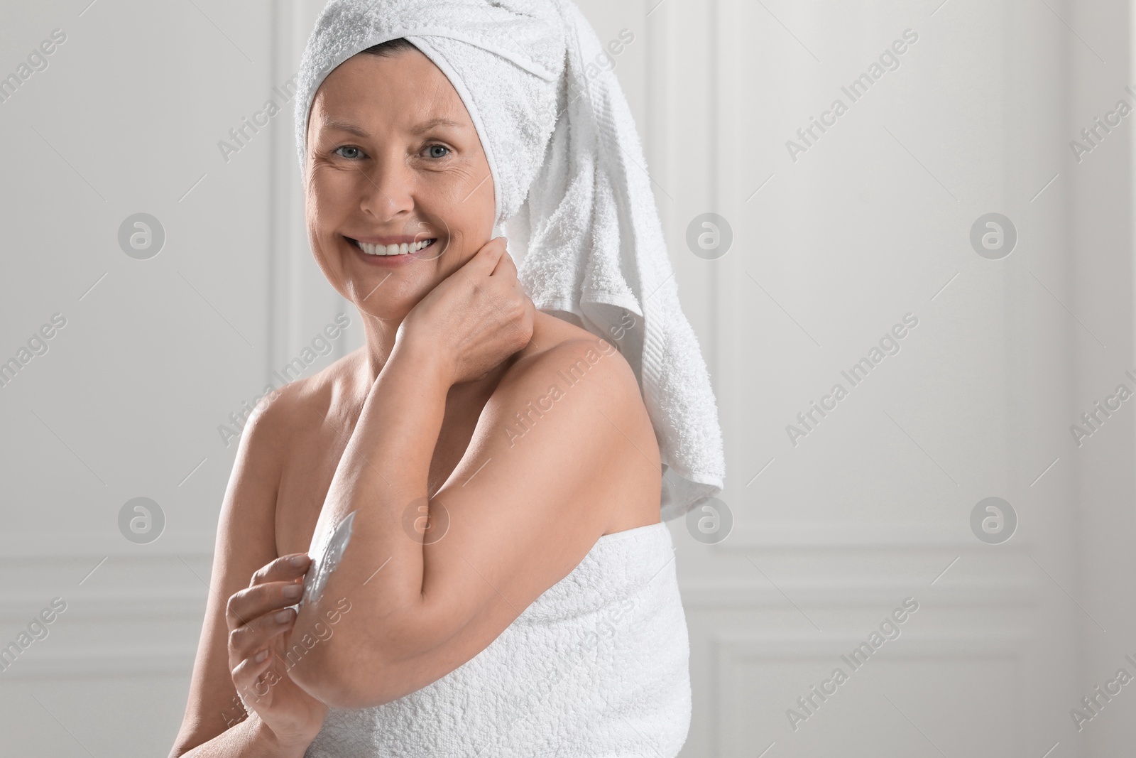 Photo of Happy woman applying body cream onto arm near white wall. Space for text
