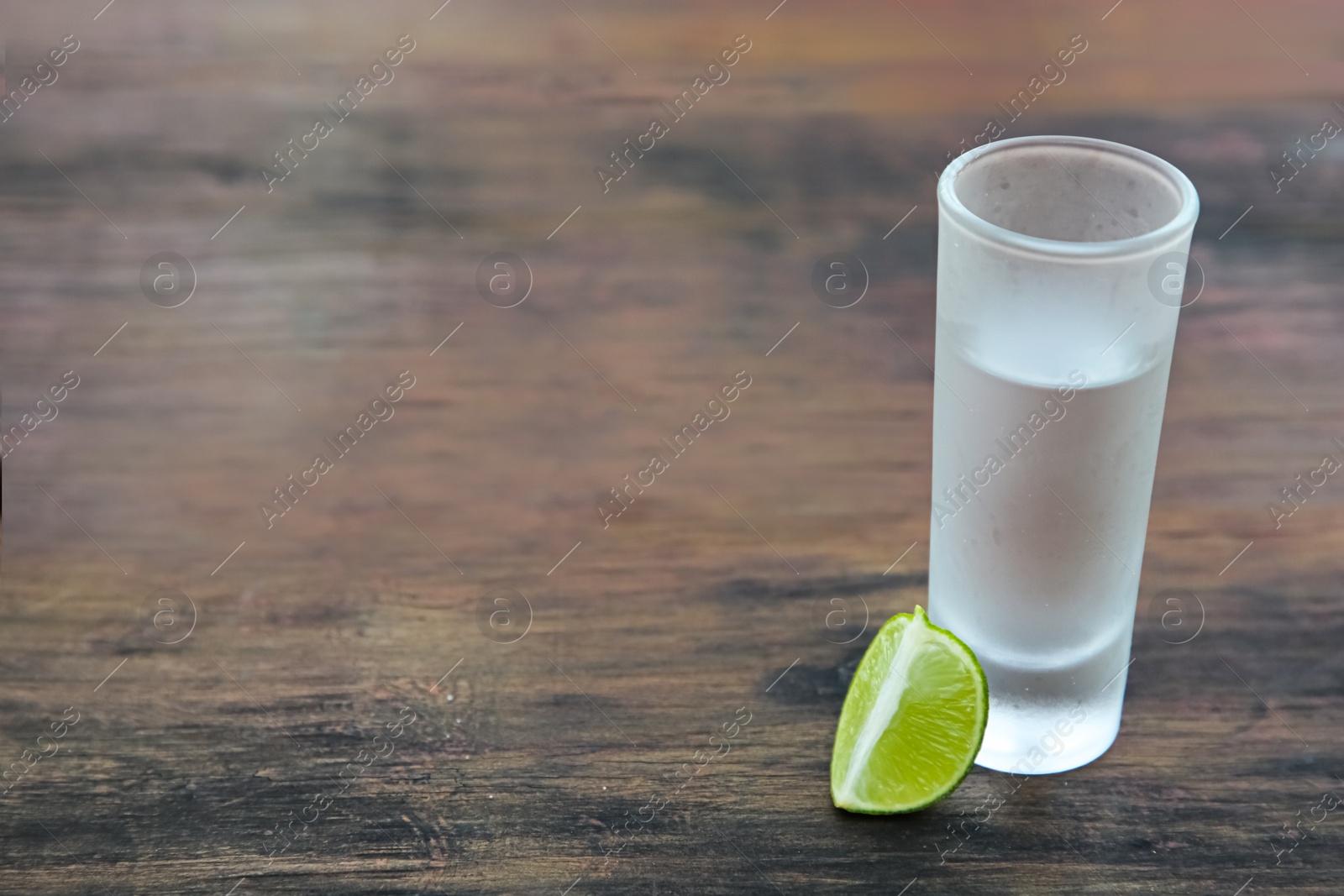 Photo of Mexican tequila shot with lime slice on wooden table, space for text. Drink made from agave