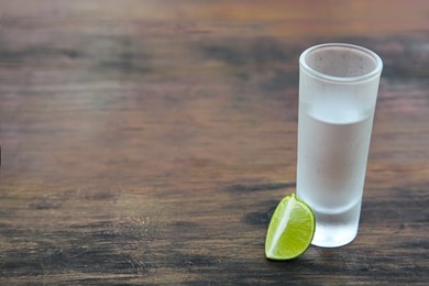 Mexican tequila shot with lime slice on wooden table, space for text. Drink made from agave