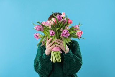 Woman covering her face with bouquet of beautiful tulips on light blue background