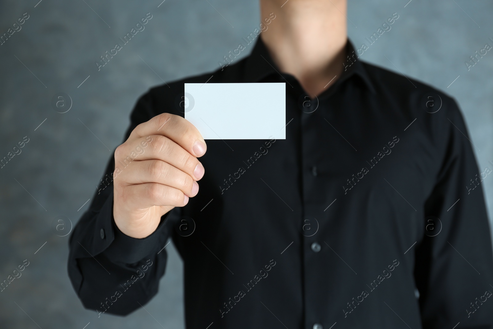 Photo of Man holding white business card on dark background, closeup