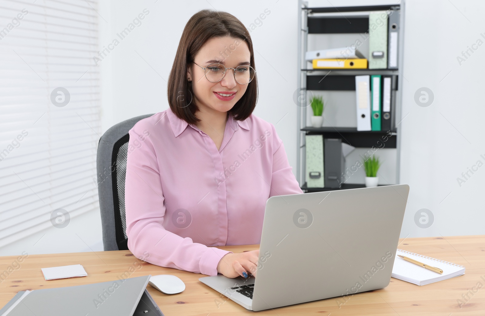 Photo of Happy young intern working with laptop at table in modern office