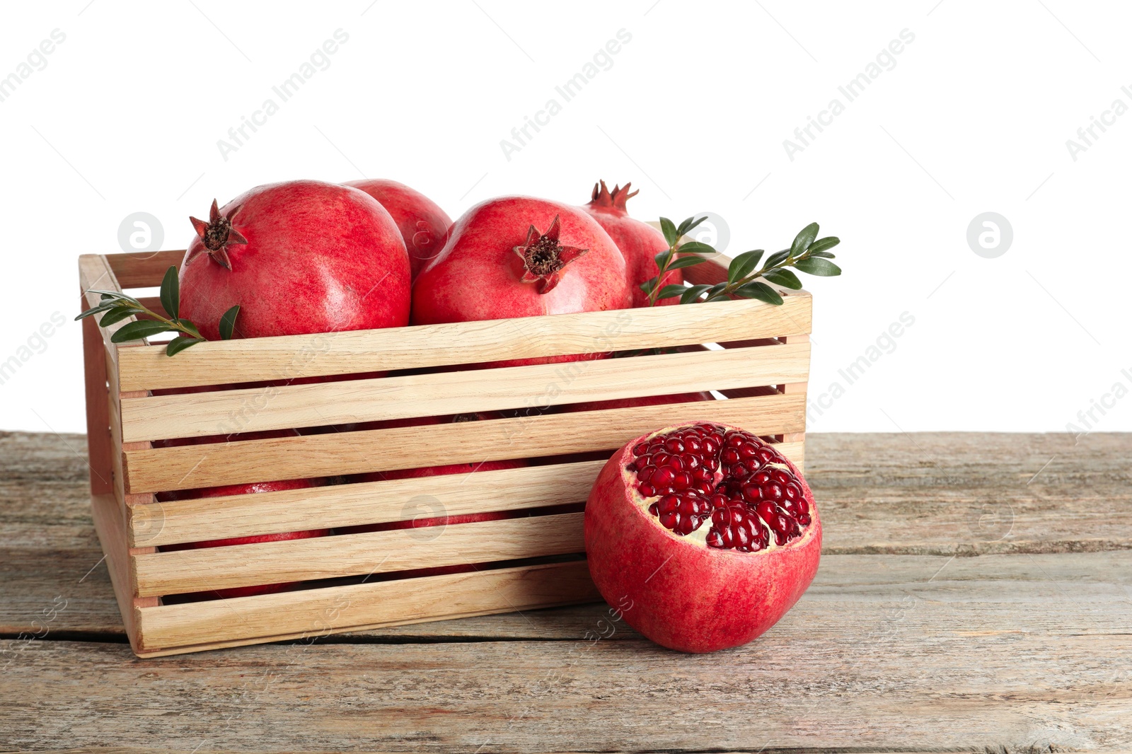 Photo of Fresh pomegranates and green leaves in box on wooden table against white background