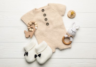 Photo of Baby pacifier, toys, knitted romper and booties on white wooden background, flat lay
