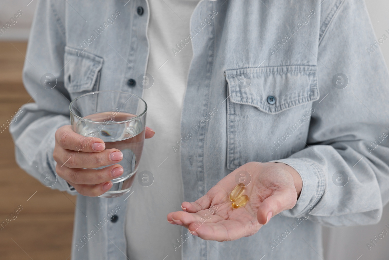 Photo of Woman with vitamin pills and glass of water indoors, closeup