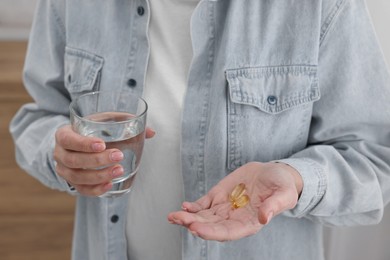 Photo of Woman with vitamin pills and glass of water indoors, closeup