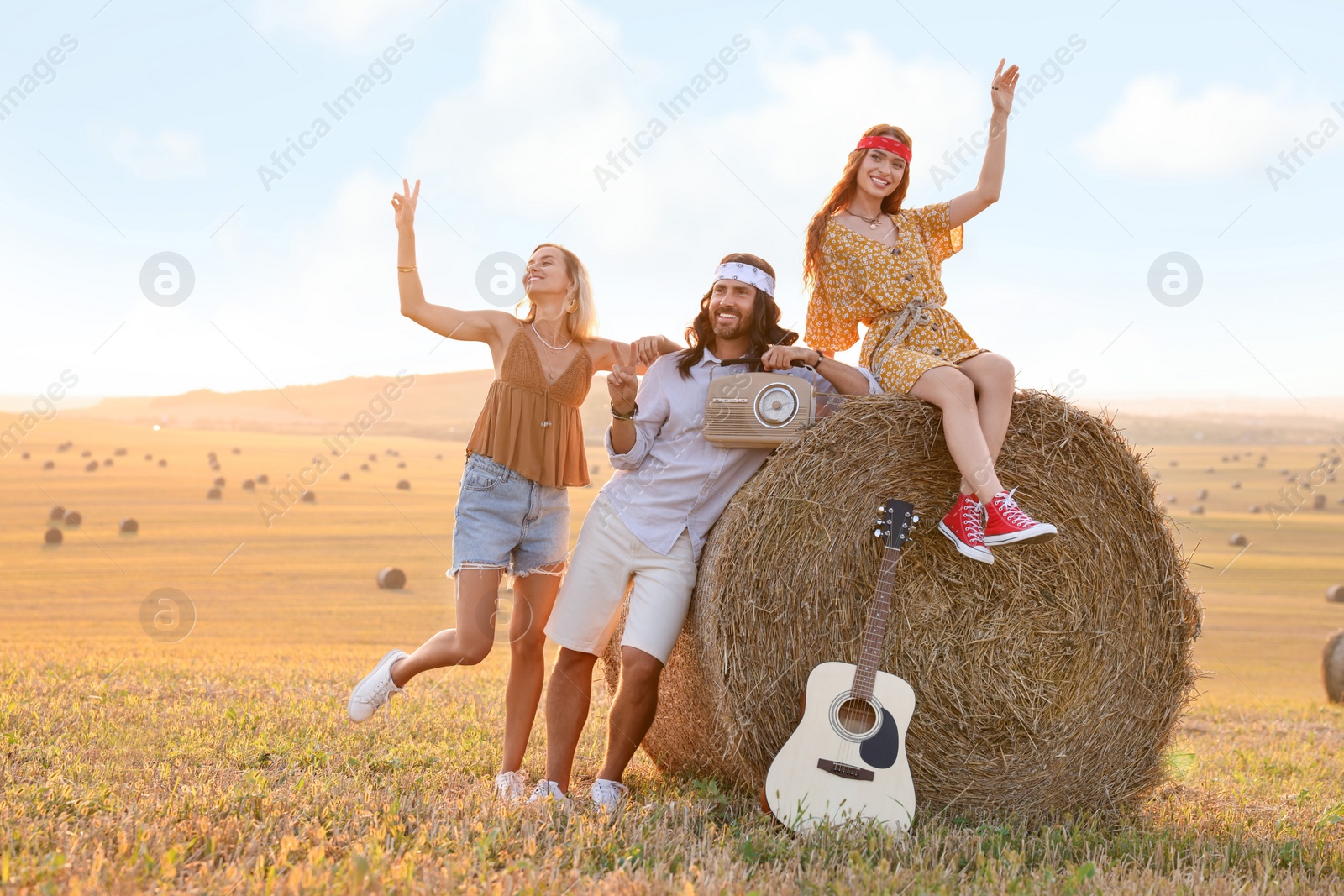Photo of Happy hippie friends with radio receiver and guitar in field, space for text