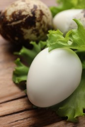 Unpeeled and peeled boiled quail eggs with lettuce on wooden table, closeup