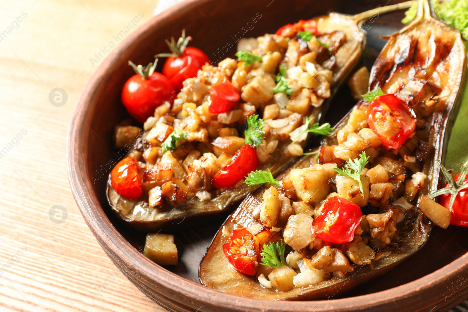 Photo of Bowl with tasty stuffed eggplants on wooden table, closeup