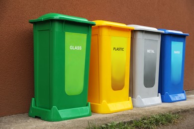 Photo of Many color recycling bins near brown wall outdoors