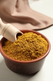 Photo of Curry powder in bowl and scoop on white table, closeup