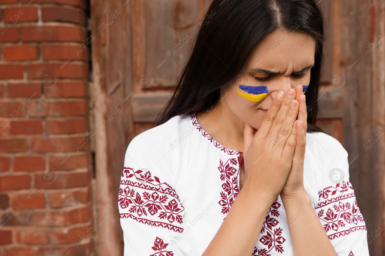 Photo of Sad young woman with drawing of Ukrainian flag on face outdoors