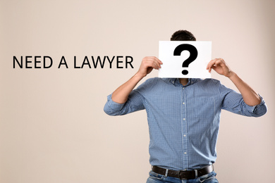 Man holding paper with question mark and text NEED A LAWYER? on beige background