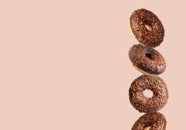 Tasty chocolate donuts with sprinkles on beige background, space for text