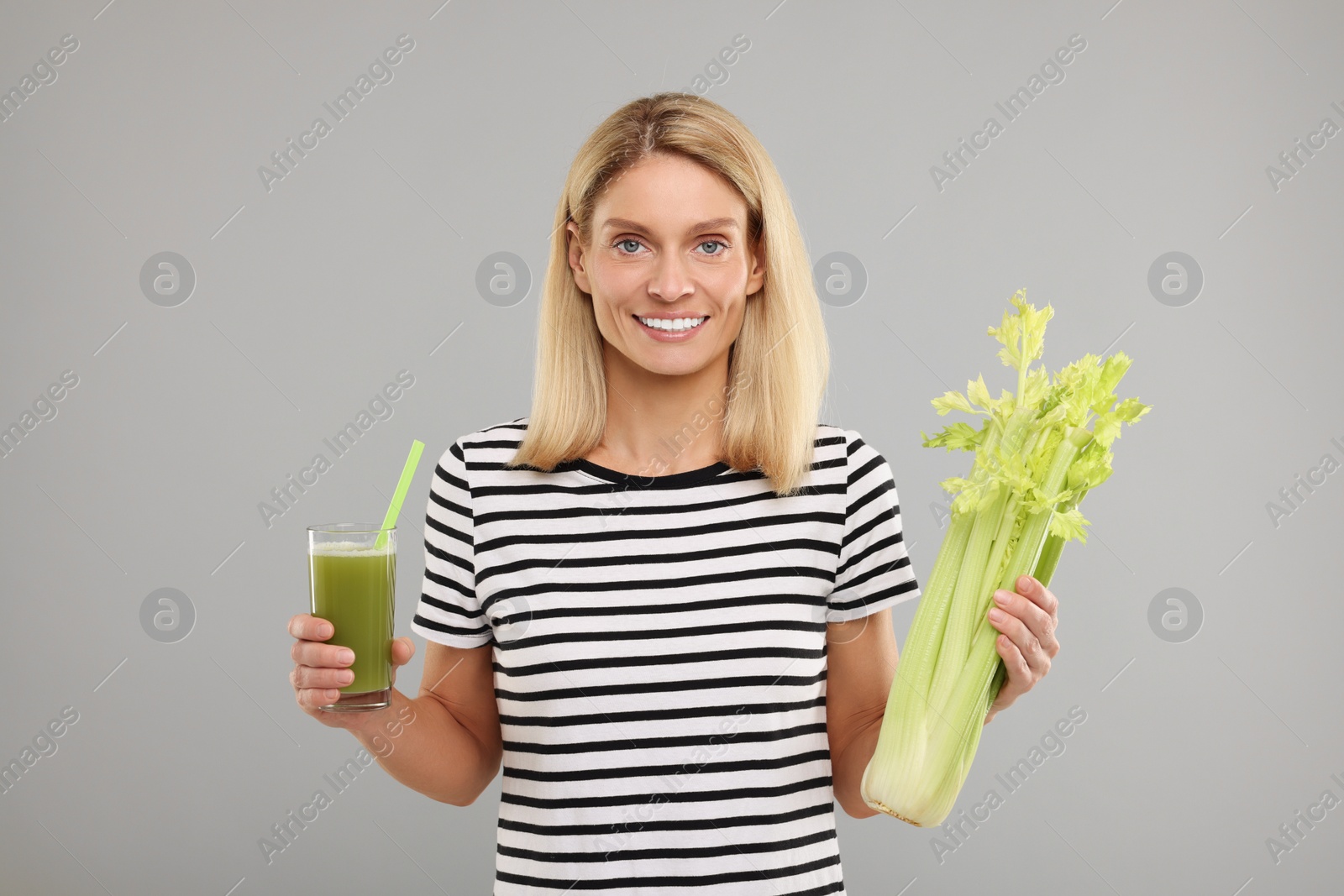 Photo of Happy woman holding glass with tasty celery juice and fresh vegetable on light grey background