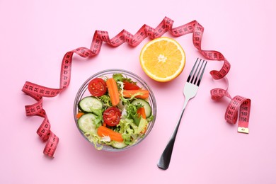 Measuring tape, salad, half of orange and fork on pink background, flat lay