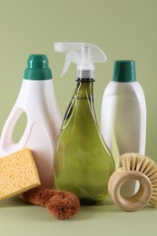 Bottles of cleaning product, brushes and sponge on light green background