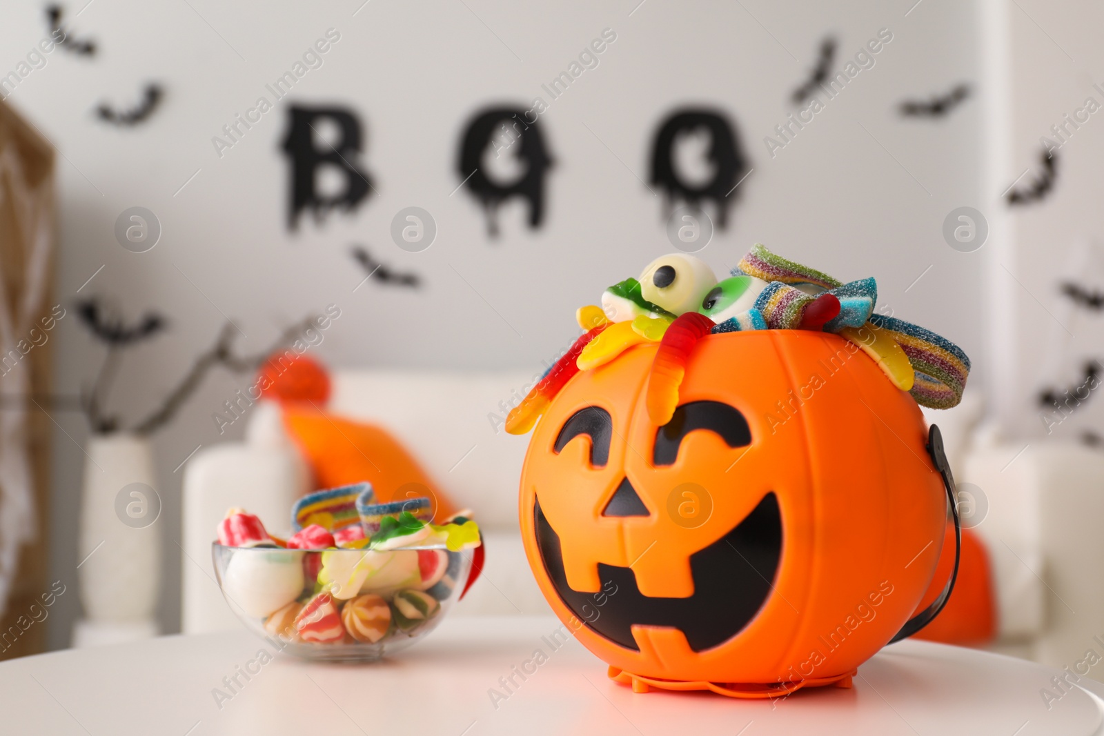 Photo of Halloween trick or treat bucket and many different sweets on white table indoors