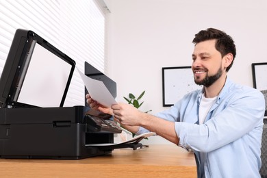 Photo of Man using modern printer at wooden table indoors