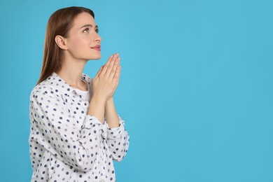 Photo of Woman with clasped hands praying on turquoise background, space for text