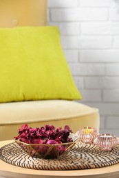 Aromatic potpourri of dried flowers in bowl and burning candles on wooden table indoors. Space for text