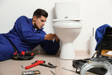 Professional plumber working with toilet bowl in bathroom