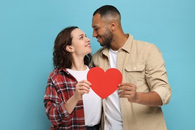 Photo of Lovely couple with red paper heart on light blue background. Valentine's day celebration