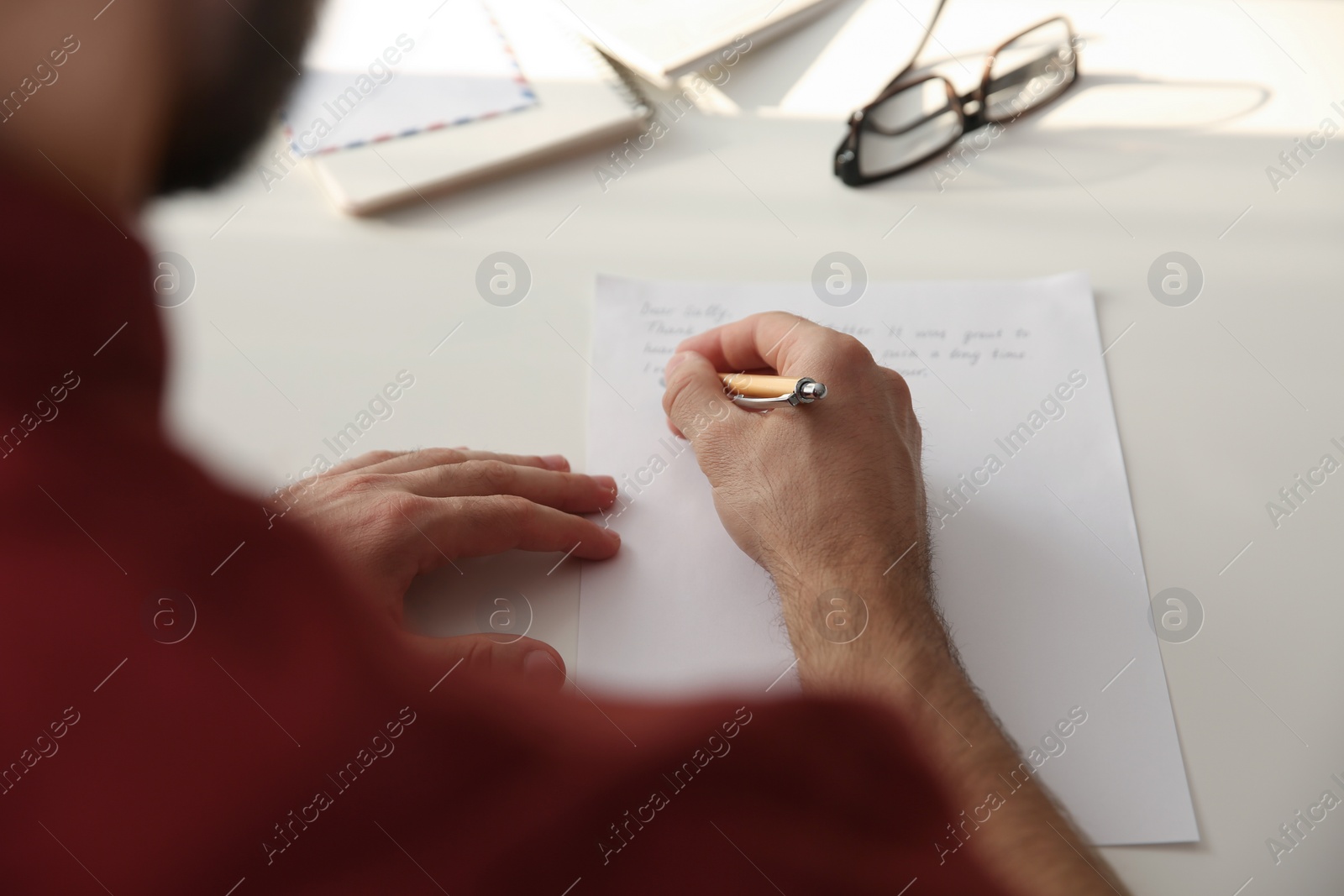 Photo of Man writing letter at white table, closeup