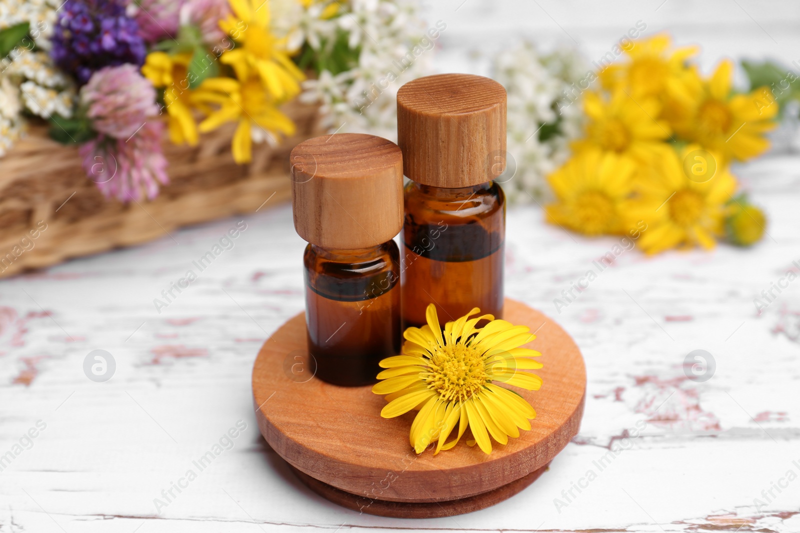 Photo of Bottles of essential oils and beautiful flowers on white wooden table