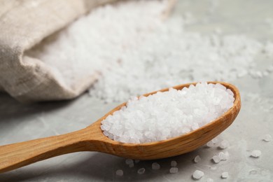 Photo of Natural sea salt in wooden spoon on light grey marble table, closeup