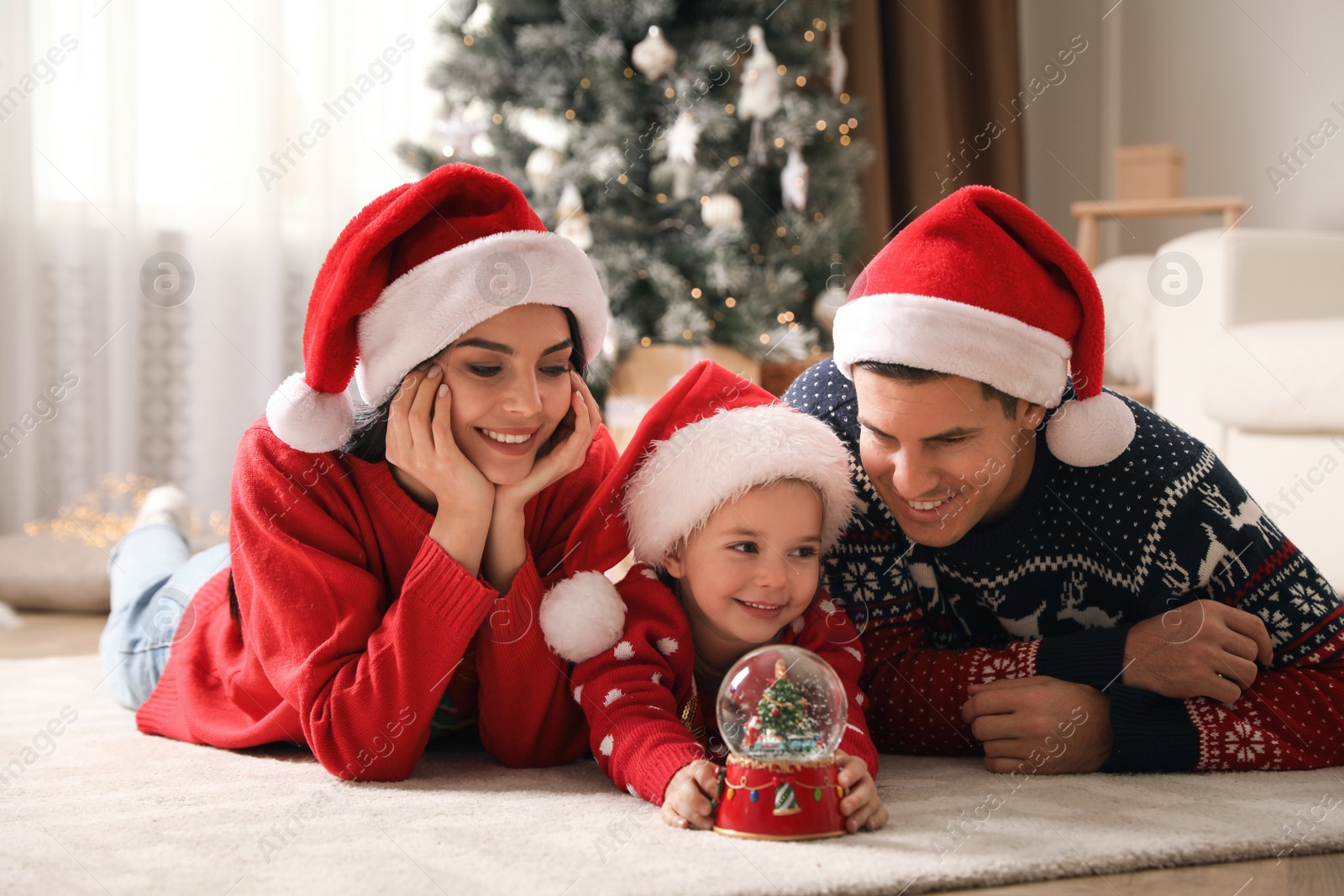Photo of Family in Santa hats playing with snow globe at home