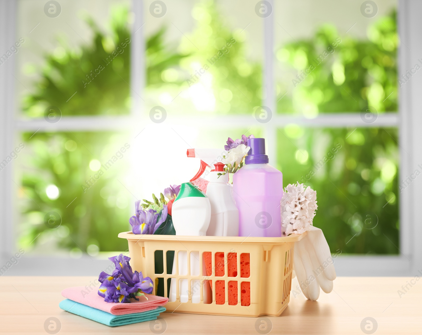 Image of Plastic basket with different detergents on wooden table indoors. Spring cleaning concept 