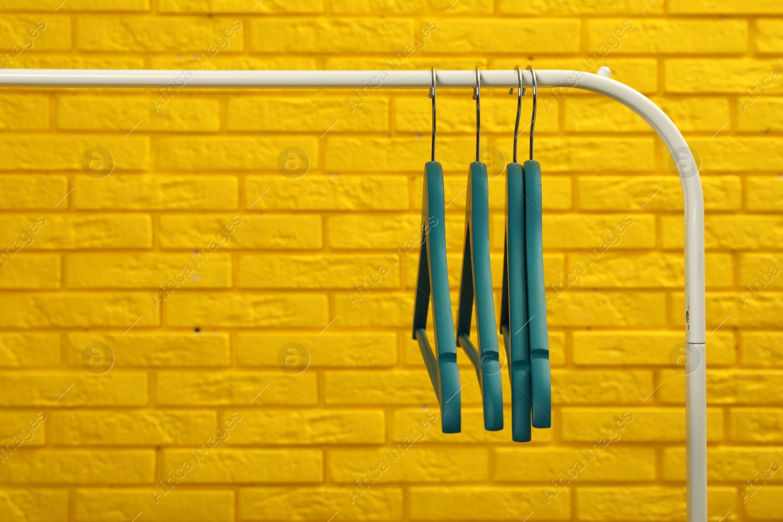 Photo of Wardrobe rack with many hangers near yellow brick wall